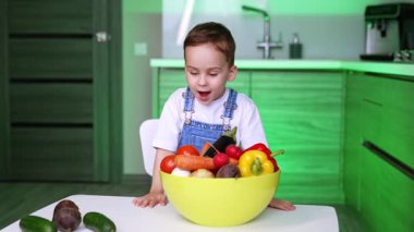 Çekici beyaz çocuk elinde çeşitli sebzelerle kasenin başında duruyor. Küçük oğlan domatesleri alıp onları gösteriyor ve gözlerine sokuyor. Çocuk sebze öğreniyor..