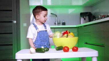 Kot pantolon giyen bebek kaseye sebze koyar. Çocuk sebzeleri ve sağlıklı beslenme alışkanlıklarını öğreniyor..