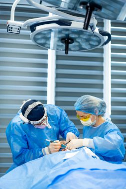 Cerrahlar ameliyathanede. Mavi önlüklü ve maskeli bir cerrahi ekip modern bir ameliyathanede ışıklar altında bir prosedür uyguluyor..