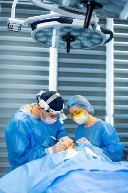 Modern hastanedeki cerrahlar. Cerrahi kıyafetli iki cerrah, iyi donanımlı bir hastane ameliyathanesinde tıbbi prosedür sırasında birlikte çalışırlar..