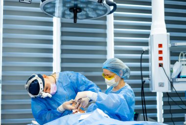 Hassas ameliyatlarda cerrahlar. Önlük ve maskeli iki yetenekli cerrah, modern bir ameliyathanede, bir hastaya odaklanmış olarak birlikte çalışırlar..