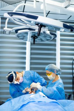 Cerrahlar steril bölgelerde ameliyat yaparlar. Mavi önlüklü iki cerrah, modern bir ameliyathanede cerrahi müdahale sırasında bir hastaya odaklanır..