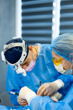 Cerrahlar hassas bir ameliyat yapıyor. Koruyucu giysili iki cerrah modern bir ameliyathanede ameliyat yaparken dikkatle odaklanıyorlar..