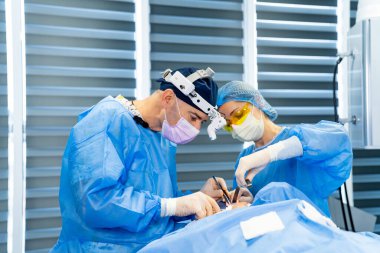 Cerrahlar ameliyathanede. Cerrahlar, tıbbi ekipmanlarla dolu, parlak ve modern bir ameliyathanede bulunan bir hastaya konsantre olurlar..