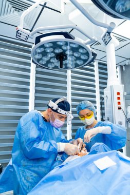 Kritik ameliyatta olan cerrahlar. Önlüklü iki cerrah, ameliyathanede parlak ışıklar altında hassas bir operasyon üzerinde ustalıkla işbirliği yapıyorlar..