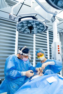 Cerrahlar ameliyathanede. Önlüklü iki cerrah, yüksek teknolojili, modern bir ameliyathanede bir hastayı ameliyat ediyor..