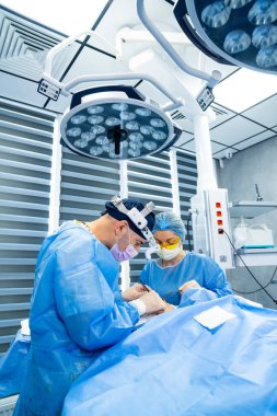 Hastanede çalışan cerrahlar. Önlüklü iki cerrah modern bir ameliyathanede cerrahi müdahaleye odaklanmış durumda..