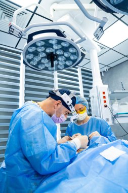 Yüksek teknolojili ameliyathanede cerrahlar. Tıp uzmanları, iyi aydınlatılmış bir ameliyathanede gelişmiş ekipmanların kullanıldığı bir cerrahi prosedüre odaklanıyor..