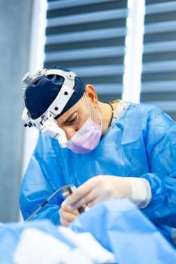 Karmaşık ameliyatta bir cerrah. Tıp profesyoneli, modern bir hastane ortamında steril bir ortamda çalışırken yoğun bir şekilde odaklanır..