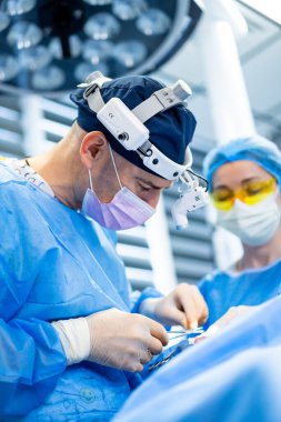 Modern bir ameliyathanede cerrahlar. Cerrahlar, iyi donanımlı bir ameliyathanede hastanın güvenliğini ve bakımını sağlama amaçlı cerrahi bir prosedüre dikkatle odaklanırlar..