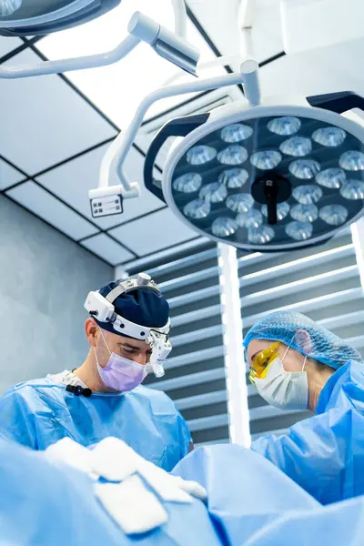 Cerrahlar modern klinikte ameliyat yaparlar. İki dişli cerrah, parlak, yüksek teknolojili bir ameliyathanede ameliyata konsantre olur..