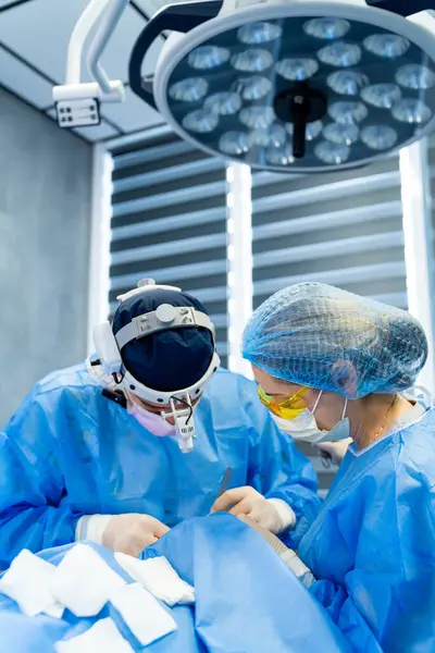 Modern ameliyathane ameliyatı. Cerrahlar iyi aydınlatılmış bir ameliyathanede özenle çalışırlar, hassas bir şekilde karmaşık bir tıbbi prosedüre odaklanırlar..