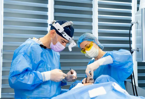 Hastanede çalışan cerrahlar. Mavi önlüklü iki cerrah, iyi donanımlı bir ameliyathanede cerrahi bir operasyon gerçekleştiriyor..