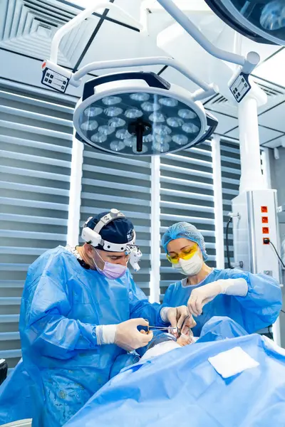 Cerrahlar ameliyathanede. Önlüklü iki cerrah, yüksek teknolojili, modern bir ameliyathanede bir hastayı ameliyat ediyor..