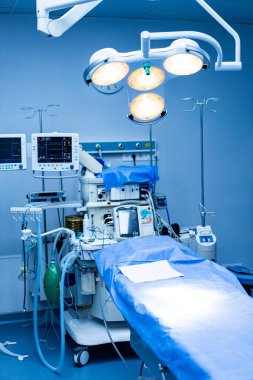 Ameliyathane ayarlandı. Steril bir ameliyathane, gelişmiş ekipman ve mavi cerrahi perdelerle cerrahi bir işlem bekliyor..