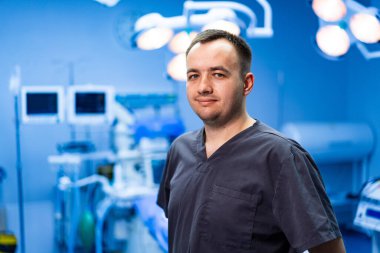 Modern ameliyathane ortamında bir cerrah. Ameliyat önlüğü giyen cerrahlar tıbbi ekipman ve ışıklarla dolu yüksek teknolojili bir ameliyathanede güvenle duruyorlar..