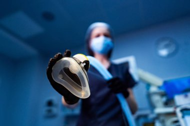 Doktor hasta bakımı için hazır. Önlüklü bir sağlık görevlisi steril bir ortamda tıbbi bir prosedüre hazırlanırken bir hava yolu cihazı tutuyor..