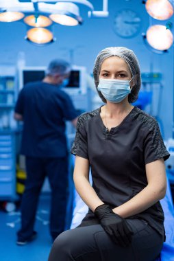 Cerrah ameliyata hazır. Cerrahi kıyafetli maskeli bir tıp uzmanı ameliyathanede ameliyata hazır bekliyor..