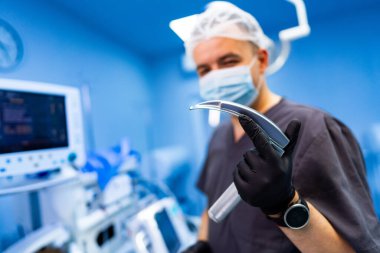 Cerrah aletleri hazırlar. Cerrah ameliyat sırasında modern bir ameliyathanede dururken cerrahi bir alet tutuyor..