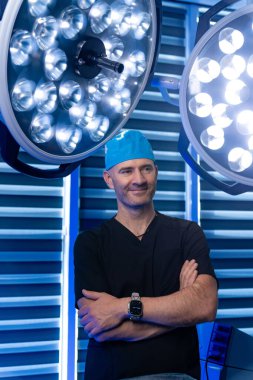 Modern ameliyathanede yetenekli bir cerrah. Kendine güvenen bir cerrah yüksek teknoloji ürünü bir ameliyathanede kollarını kavuşturup ileri düzey ışıklandırma ve ekipman sergiliyor..