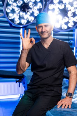 Cerrah ameliyathaneden memnun. Önlüklü yetenekli bir cerrah güvenli bir şekilde poz verir. Parlak ışıklı bir ameliyathane ortamında onay sinyali verir..