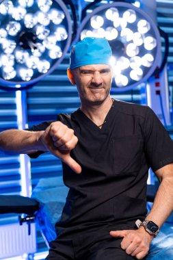 Doktor ameliyatta hayal kırıklığına uğradı. Önlüklü bir cerrah, parlak ve steril bir ameliyathanede hayal kırıklığını gösteren baş parmak hareketi yapar..