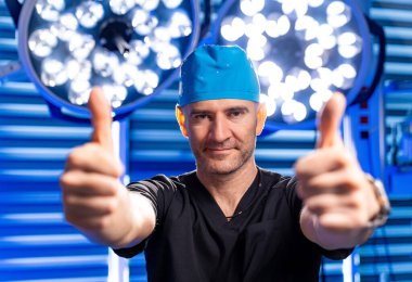 Cerrah ameliyathanede. Cerrah, ameliyat şapkası ve önlüğü takıp kendine güveni yükseltirken iyi aydınlatılmış bir ameliyathanede onay veriyor..