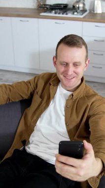 Kanepede oturup selfie çeken mutlu bir adam. Modern evde selfie çeken yakışıklı bir adam. Dikey video