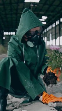 Koruyucu üniformalı bir insan tehlikeli bir şehre çiçek dikiyor. Koruyucu giysili ve gözlüklü adam. Dikey video