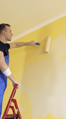 Genç ressam ev tadilatı yapıyor. Yeni duvar boyayan yakışıklı bir işçi. Dikey video