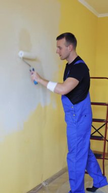 Boyalı pateniyle yakışıklı adam yeni bir iç mekan geliştirmesi yapıyor. Profesyonel inşaatçı tadilatı. Dikey video