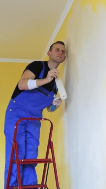 Yeni apartman yenileme odasında genç bir adam. Evi yenilemek için fırça fırçasıyla çalışan yakışıklı bir ressam. Dikey video