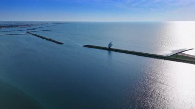 Markermeer Gölü 'nün kenarındaki barajlar güneşte parlıyor. Suyun üzerinde oturan insanın demir figürüne yaklaşıyoruz. Lelystad, Hollanda.