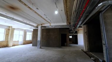 Tamamlanmamış duvarları, tavanı ve zemini olan uçsuz bucaksız odada. Önermenin tavanındaki boruların düşük açılı görüntüsü. Yenileme konsepti.