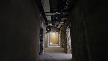 Binanın içindeki uzun koridorda yeniden inşa ediliyor. Koridor boyunca kapısı olmayan kapılar var. Tavandaki borular ve kablolar. Düşük açı görünümü.