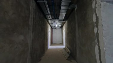 Tamamlanmamış duvarları olan yenilenmiş binanın koridoru. Tavandaki boruların sistemi. Düşük açı görünümü.