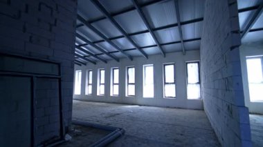 Geniş tavan arasına giriyorlar. Dar pencereler ve tuğla duvarlar var. Yeni binanın içi..