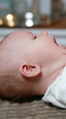 Güzel beyaz bir bebek sırt üstü uzanmış esniyor. Sevimli küçük erkek bebek çok güzel hapşırıyor. Yan görünüş yakın. Dikey video