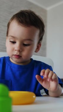 Beyaz masada oturan Kafkasyalı bir erkek bebek. Küçük çocuk oyuncak piramidiyle oynuyor. Dikey video