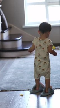 Odada annesinin terliklerini giymiş küçük bir bebeğin yürüme görüntüsü. Çocuk yavaş hareket ederek küçük adımlar atıyor. Dikey video