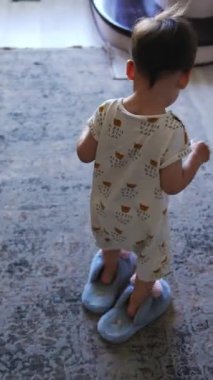 Büyük terlikler giyen komik küçük çocuğu takip ediyorum. Çocuk merdivenlere çıkıyor ve bir basamağa oturup ayakkabılarını çıkarıyor. Üst Manzara. Dikey video