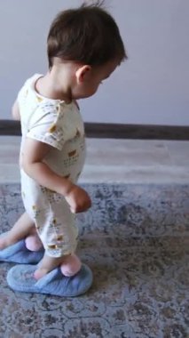 Mavi pofuduk terlik giyen sevimli küçük çocuk odanın bir ucundan diğerine geçiyor. Çocuk annesinin ayakkabılarını ödünç aldı. Dikey video