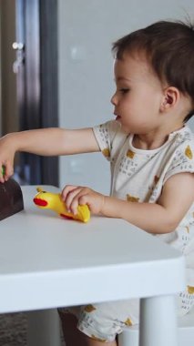 Küçük masada oynayan mutlu, aktif bir çocuk. Çocuk plastik kuşu alıp masaya çarpmış. Dikey video