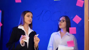 Beyaz kadınlar cam duvarda sayıları tartışıyor. Meslektaşlar fikirleri paylaşır, strateji oluşturur ve plan yapar..