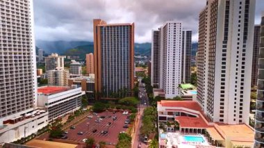 Otoparkın üstündeki yüksek binaların arasında uçmak. Yağmur bulutları arka planda dağların üzerinde toplanır. Honolulu, Oahu, Hawaii, ABD.