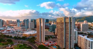 Waikiki, Honolulu, Hawaii, ABD 'deki yüksek binaların tepelerine yaklaşıyoruz. Drone 'dan şehrin gün batımına doğru. Şehir zemininde pofuduk bulutlu bir manzara.