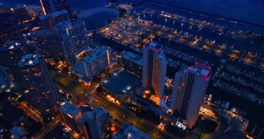 Alacakaranlıkta güzel aydınlatılmış modern şehir. Honolulu, Hawaii, ABD ve yakınındaki yat kulübünün çarpıcı su manzarasının en üst görüntüsü..