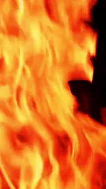 Kamp ateşinde parlayan alevli turuncu. Karanlık arka planda alevler. Dikey video