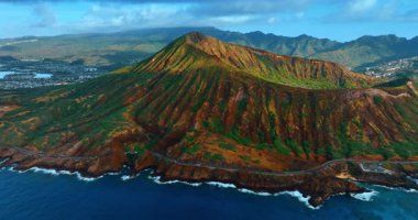 Karayolu boyunca ilerleyen araç, su manzarasının üstündeki yırtık pırtık dağların manzaralı yamacından geçiyor. İnsansız hava aracı görüntüleri Honolulu, Hawaii, ABD 'deki çarpıcı Diamond Head Krateri' ne yaklaşıyor..