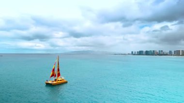 Su yüzeyinde kırmızı-sarı yelkenli sevimli sarı tekne. Honolulu, Hawaii, ABD kıyılarında yelken açtı. Hava görünümü.